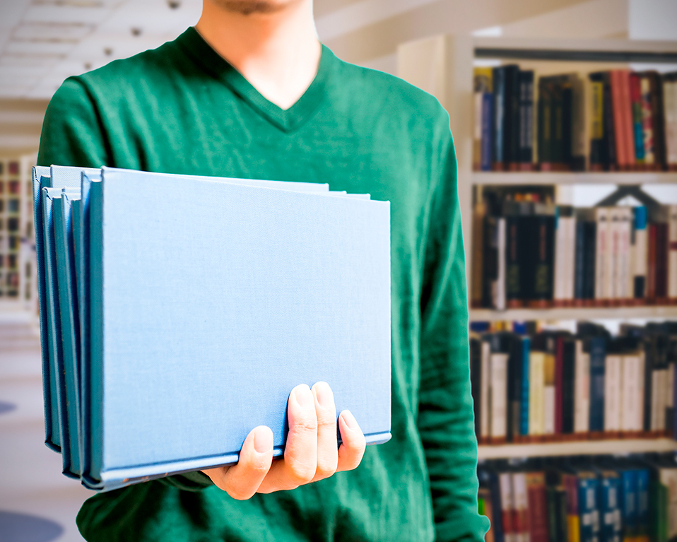 Primer plano de un estudiante sujetando diversos libros de tapa azul en una de las bibliotecas de la Universidad de Granada