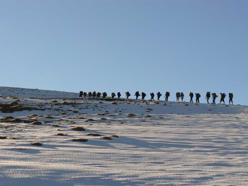 Un numeroso grupo de personas, inicia el ascenso de la ladera de una montaña nevada